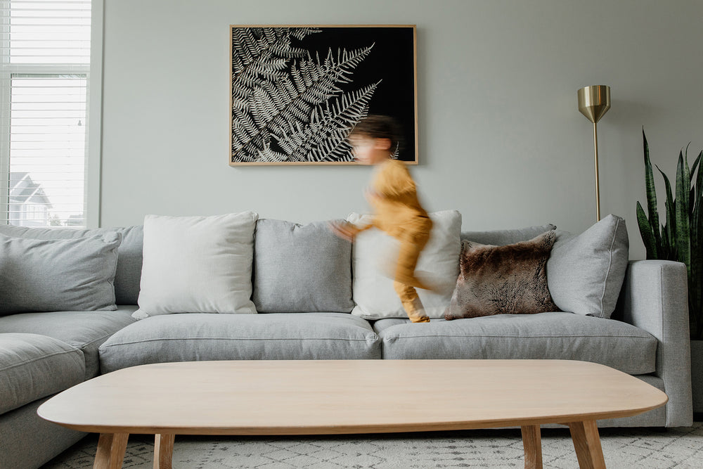 Large Scale Premium Floral Wall Art in a cozy, comfortable and warm interior design space. The premium quality of the paper elevates the floral designs that are photographed and hung in the living room. There is a child running across the couch in front. 