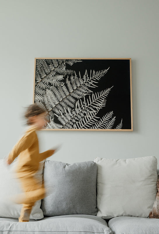 Large Scale Premium Floral Wall Art in a cozy, comfortable and warm interior design space. The premium quality of the paper elevates the floral designs that are photographed and hung in the living room. Blurred child in motion in the foreground.